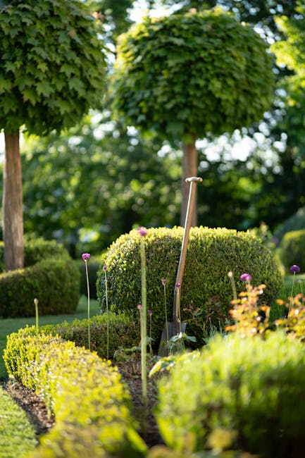 A spacious nursery garden at Mottingham Station, featuring multiple raised wooden beds filled with a variety of potted plants, including shrubs, flowering plants, and small trees. The plants display f